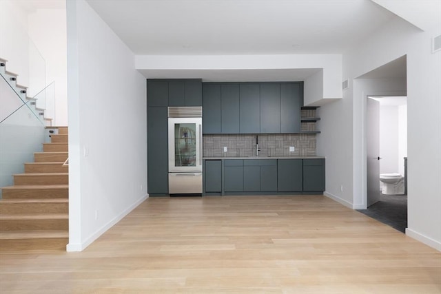 kitchen with gray cabinets, decorative backsplash, open shelves, light wood finished floors, and stainless steel built in refrigerator