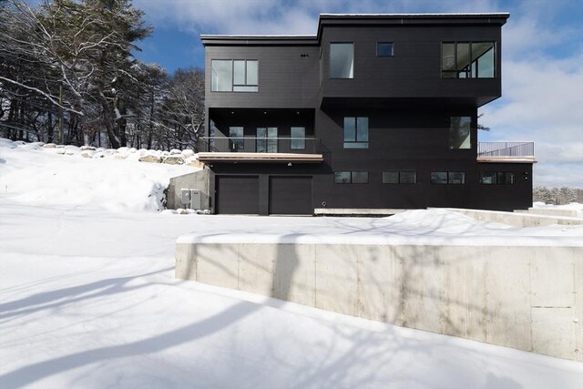 snow covered back of property with a balcony and an attached garage