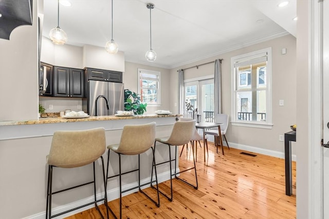 kitchen featuring visible vents, a breakfast bar, freestanding refrigerator, crown molding, and light wood-type flooring