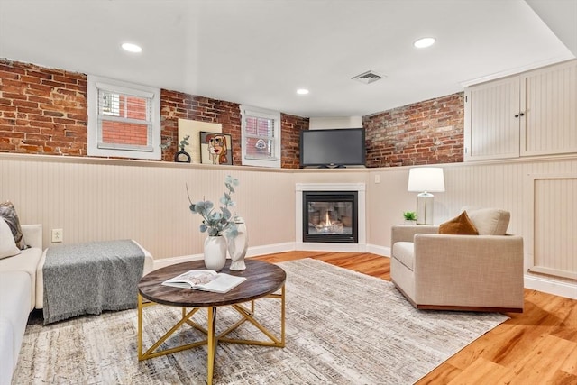 living area featuring light wood-style floors, visible vents, a wainscoted wall, and a glass covered fireplace