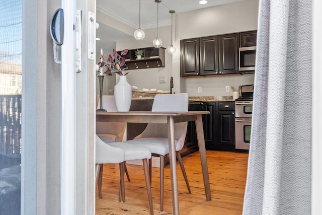 kitchen with pendant lighting, crown molding, light wood finished floors, appliances with stainless steel finishes, and dark brown cabinets