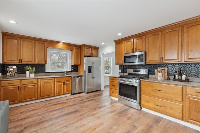 kitchen featuring appliances with stainless steel finishes, sink, decorative backsplash, and light wood-type flooring