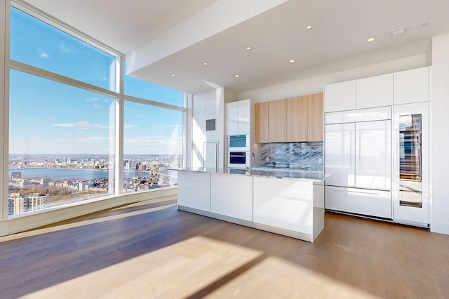 kitchen featuring paneled refrigerator, a healthy amount of sunlight, wood-type flooring, and white cabinets