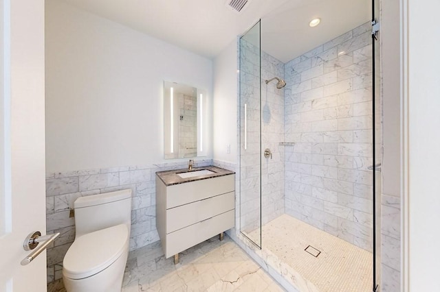 bathroom with tiled shower, vanity, toilet, and tile walls