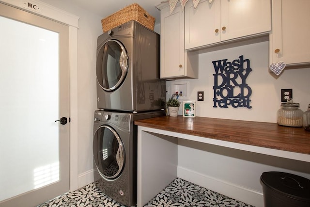 washroom featuring stacked washer and clothes dryer, cabinet space, baseboards, and tile patterned floors