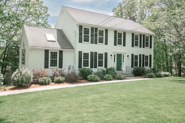 colonial-style house with roof with shingles, a front yard, and a chimney