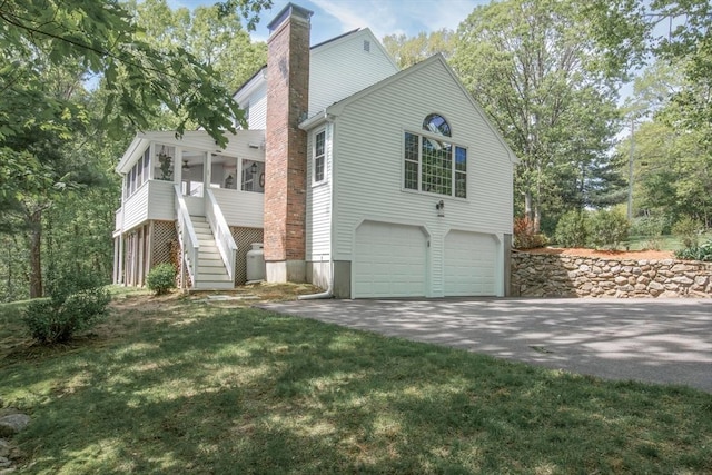 view of side of property featuring a chimney, stairs, an attached garage, a sunroom, and asphalt driveway