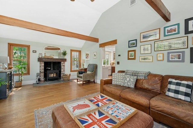 living area with a wood stove, wood finished floors, beam ceiling, baseboards, and high vaulted ceiling