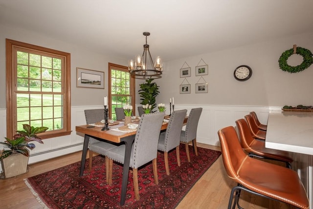 dining area featuring a chandelier, wood finished floors, a wainscoted wall, a decorative wall, and a baseboard heating unit