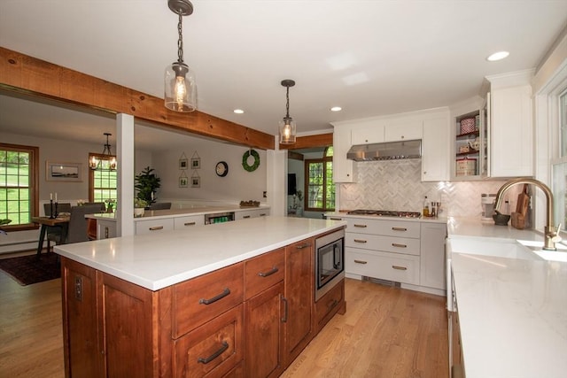 kitchen featuring appliances with stainless steel finishes, light wood-style flooring, under cabinet range hood, white cabinetry, and tasteful backsplash