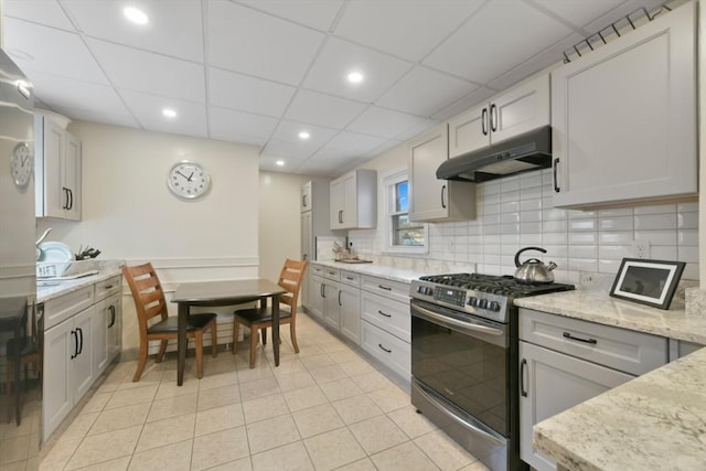 kitchen with a paneled ceiling, light stone countertops, light tile patterned floors, and stainless steel gas range