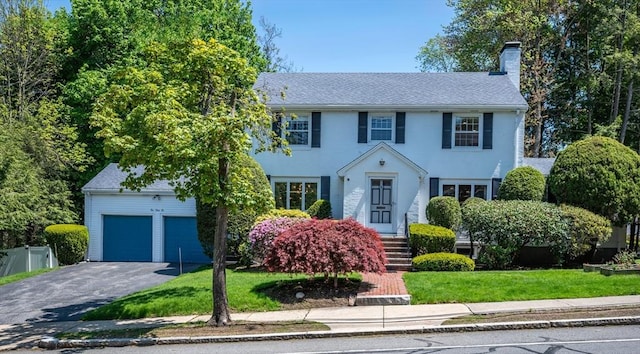 colonial-style house featuring a chimney, asphalt driveway, and a front lawn