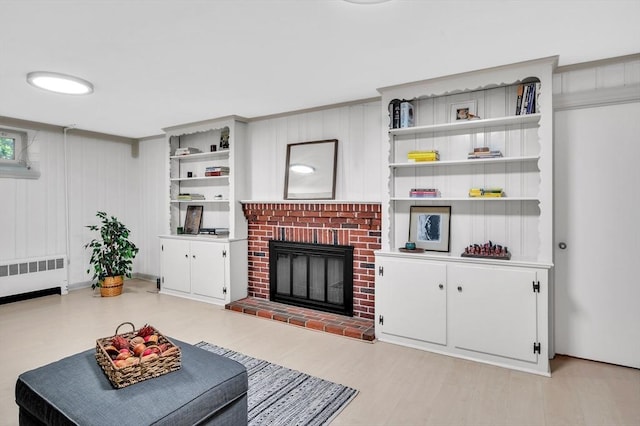 living area with radiator, light wood finished floors, and a brick fireplace