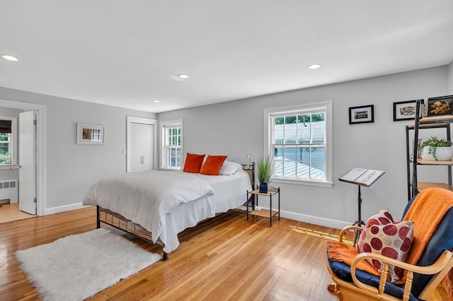 bedroom with radiator heating unit, multiple windows, light wood finished floors, baseboards, and recessed lighting