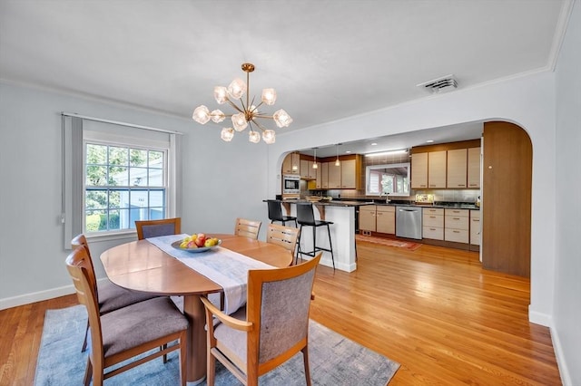 dining room featuring arched walkways, light wood-type flooring, a chandelier, baseboards, and ornamental molding
