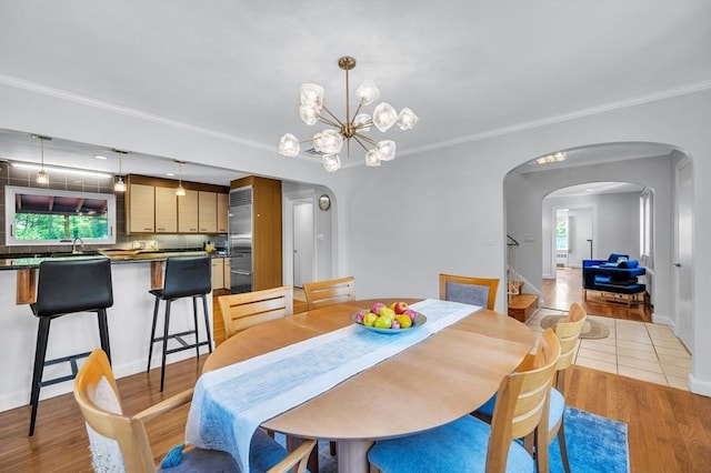 dining room featuring arched walkways, light wood finished floors, ornamental molding, a chandelier, and baseboards