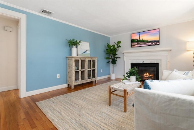 living room with wood finished floors, visible vents, baseboards, ornamental molding, and a glass covered fireplace