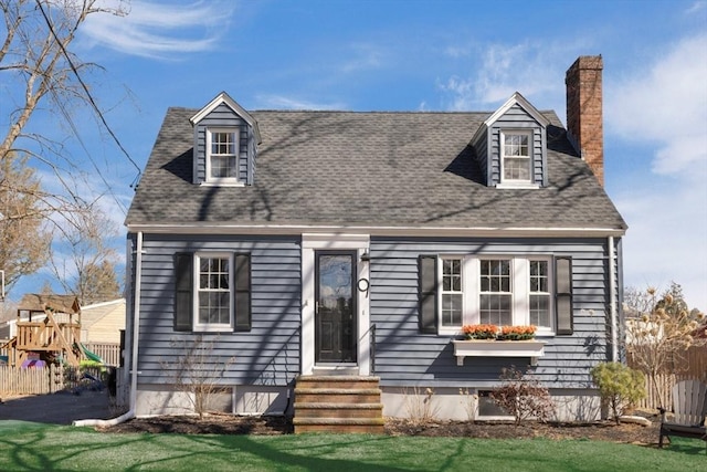 new england style home with a playground, roof with shingles, a chimney, and fence