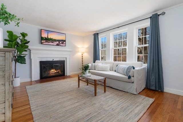 living room with baseboards, a fireplace with flush hearth, light wood-style floors, and crown molding