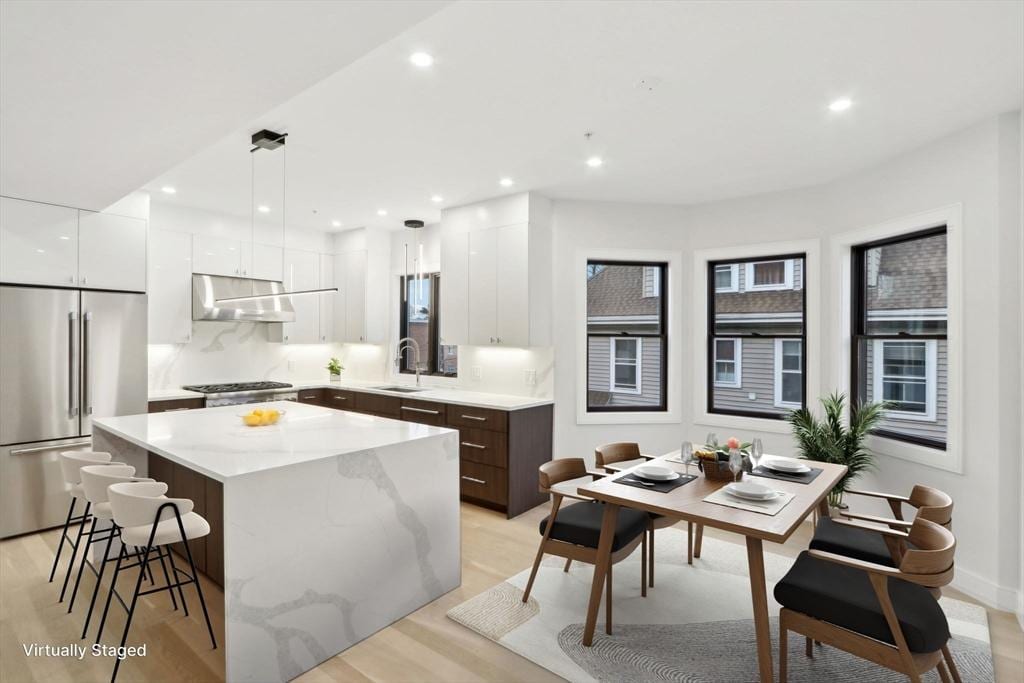 kitchen featuring white cabinetry, a center island, stainless steel appliances, light hardwood / wood-style floors, and decorative light fixtures