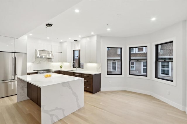 kitchen featuring appliances with stainless steel finishes, light wood-type flooring, dark brown cabinets, a center island, and hanging light fixtures