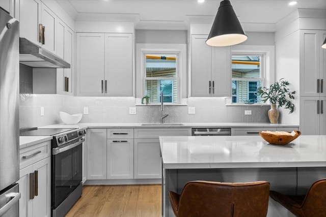 kitchen with a kitchen breakfast bar, under cabinet range hood, a sink, stainless steel appliances, and light wood finished floors