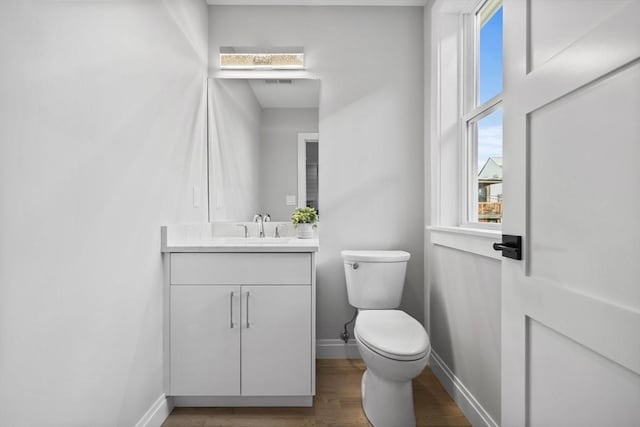 half bath featuring vanity, baseboards, toilet, visible vents, and wood finished floors