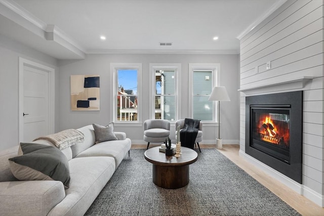 living area featuring crown molding, visible vents, a large fireplace, and wood finished floors