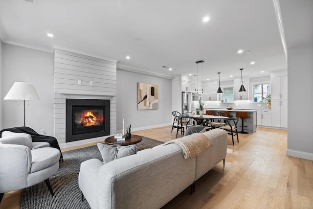 living room featuring crown molding, a large fireplace, recessed lighting, light wood finished floors, and baseboards
