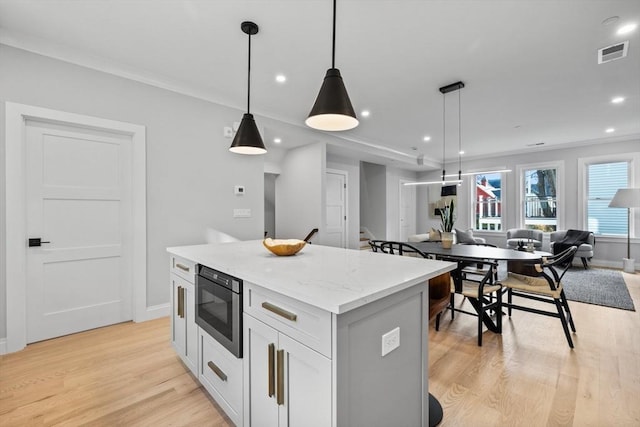 kitchen with black microwave, light wood-type flooring, visible vents, a kitchen island, and open floor plan