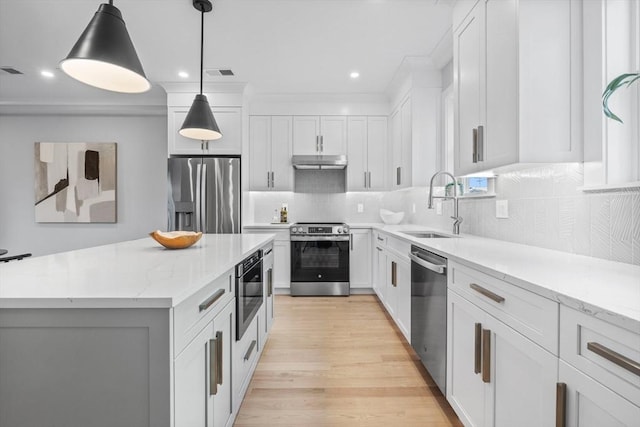 kitchen with tasteful backsplash, under cabinet range hood, appliances with stainless steel finishes, light wood finished floors, and a sink