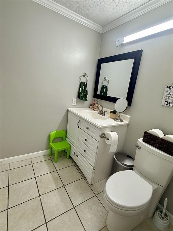 bathroom with toilet, vanity, tile patterned floors, crown molding, and a textured ceiling