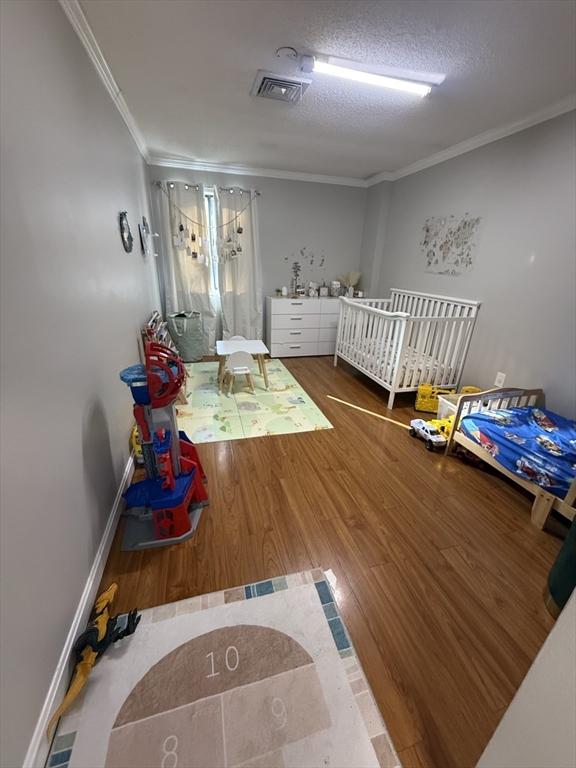 unfurnished bedroom featuring wood-type flooring, a crib, ornamental molding, and a textured ceiling