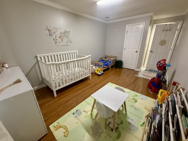 bedroom with a crib, ornamental molding, and hardwood / wood-style floors