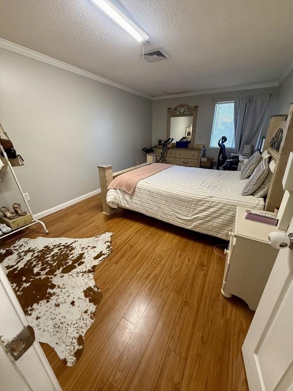 bedroom featuring a textured ceiling, ornamental molding, and hardwood / wood-style floors