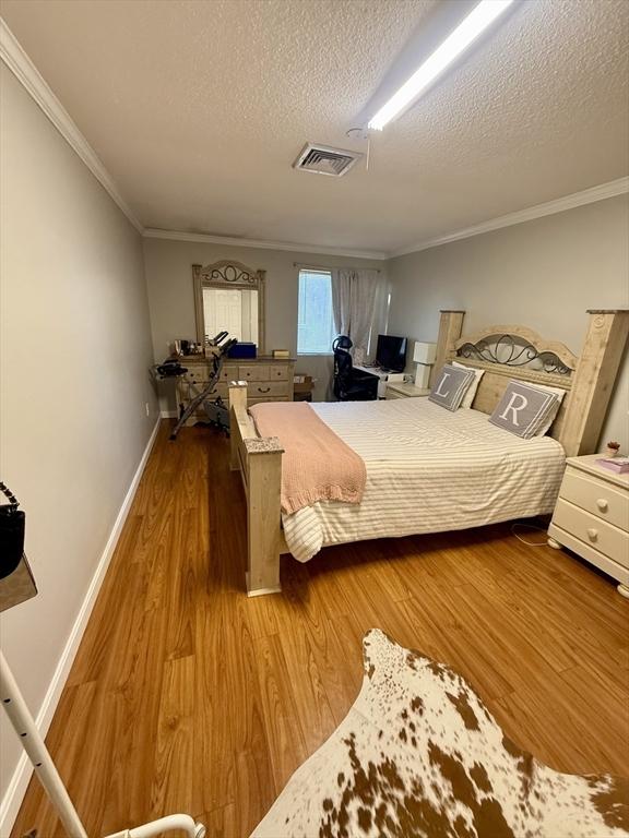 bedroom featuring wood-type flooring, a textured ceiling, and crown molding