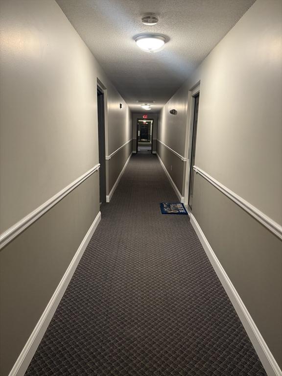 hall with a textured ceiling and dark colored carpet