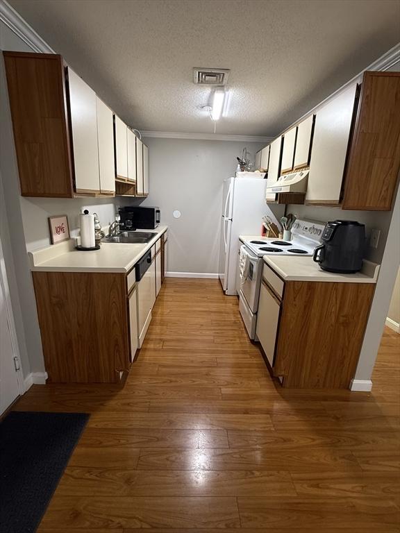 kitchen featuring white appliances, a textured ceiling, ornamental molding, light hardwood / wood-style flooring, and sink