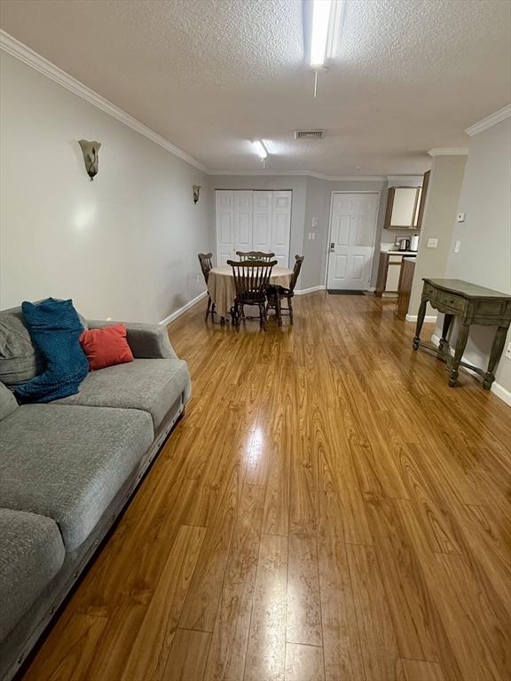 living room featuring ornamental molding, a textured ceiling, and light hardwood / wood-style flooring