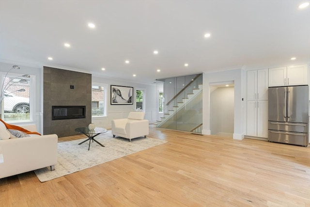 unfurnished living room featuring ornamental molding, light wood finished floors, stairway, and a tiled fireplace