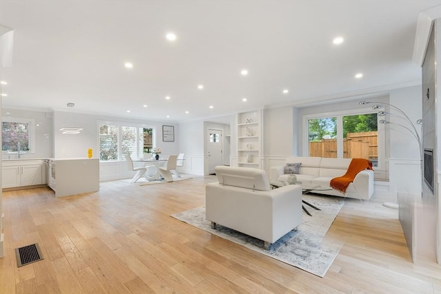 living room with light wood-type flooring, visible vents, and ornamental molding