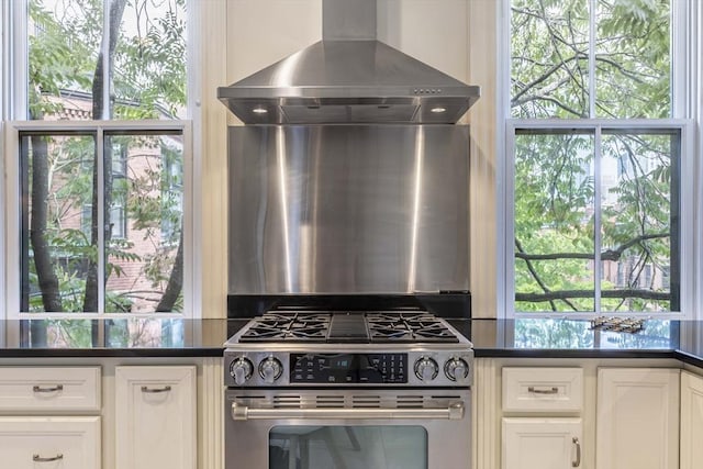 kitchen with stainless steel range with gas stovetop, plenty of natural light, and wall chimney range hood