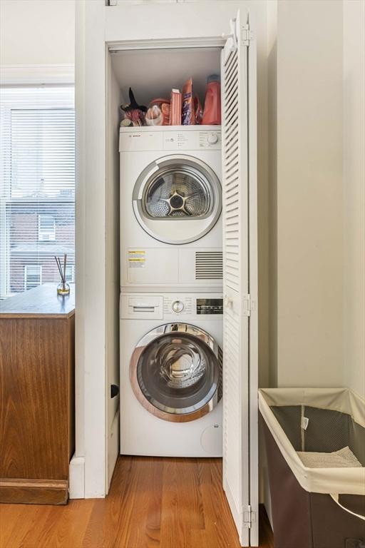 clothes washing area with hardwood / wood-style flooring and stacked washer and clothes dryer