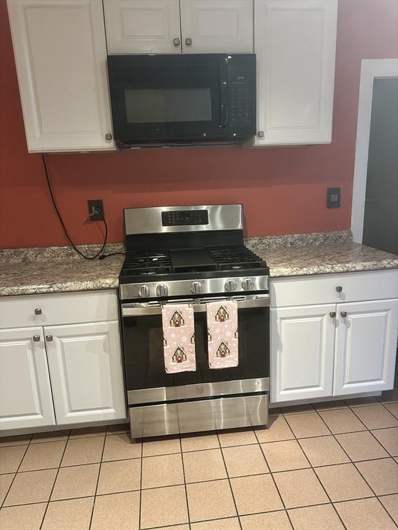 kitchen with stainless steel range with gas cooktop, white cabinets, and light tile patterned floors