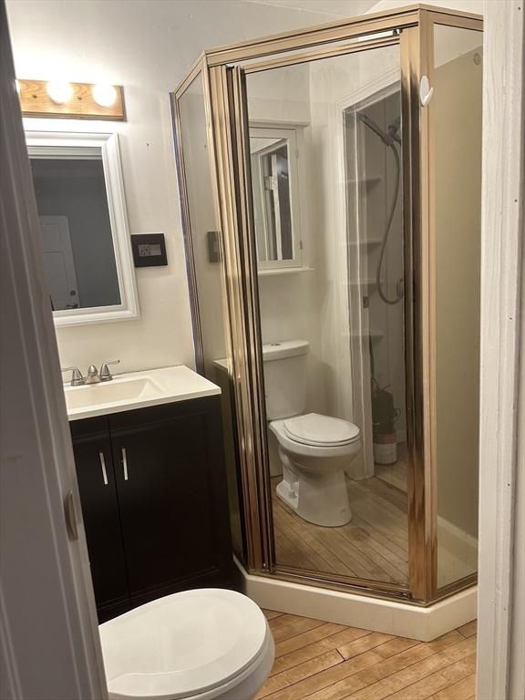 bathroom with a shower with door, vanity, wood-type flooring, and toilet