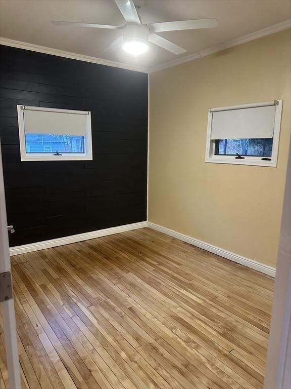 empty room with wood walls, ornamental molding, and light wood-type flooring