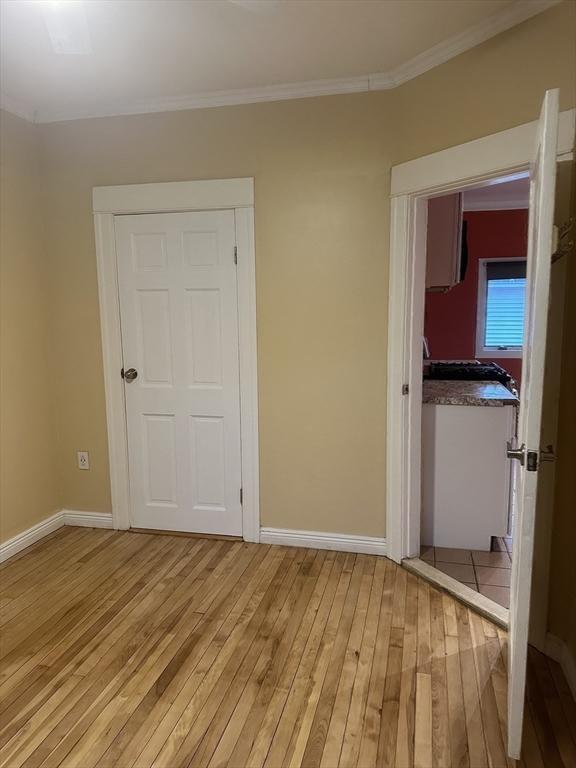 unfurnished bedroom with light wood-type flooring, crown molding, and a closet