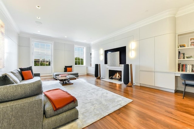 living area with a fireplace with flush hearth, wood finished floors, and crown molding