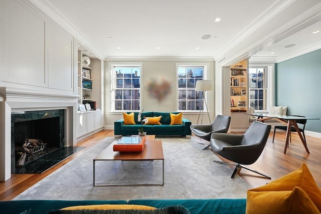 living area featuring ornamental molding, built in shelves, light wood-style floors, and a premium fireplace