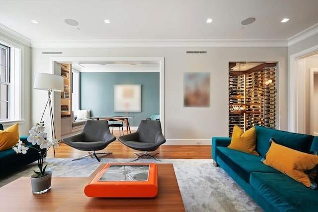 living area with baseboards, wood finished floors, visible vents, and ornamental molding